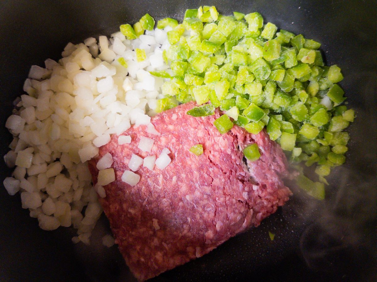 Chopped frozen peppers, chopped frozen onion, and ground beef in a pot on the stove.
