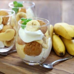 Mini Banana Pudding Cups and some ripe bananas on a table with a spoon.