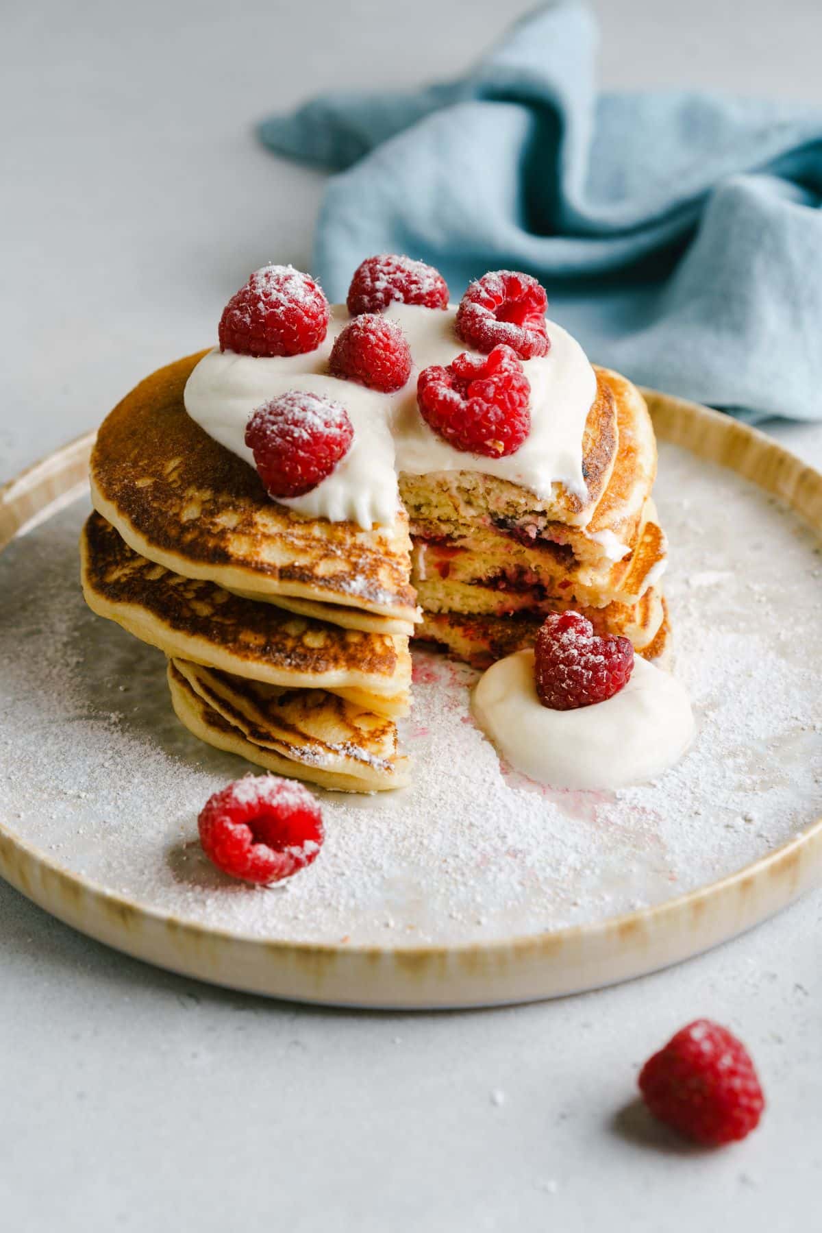 A stack of pancakes with fruit and cream sauce on a plate, cut into about to be eaten.