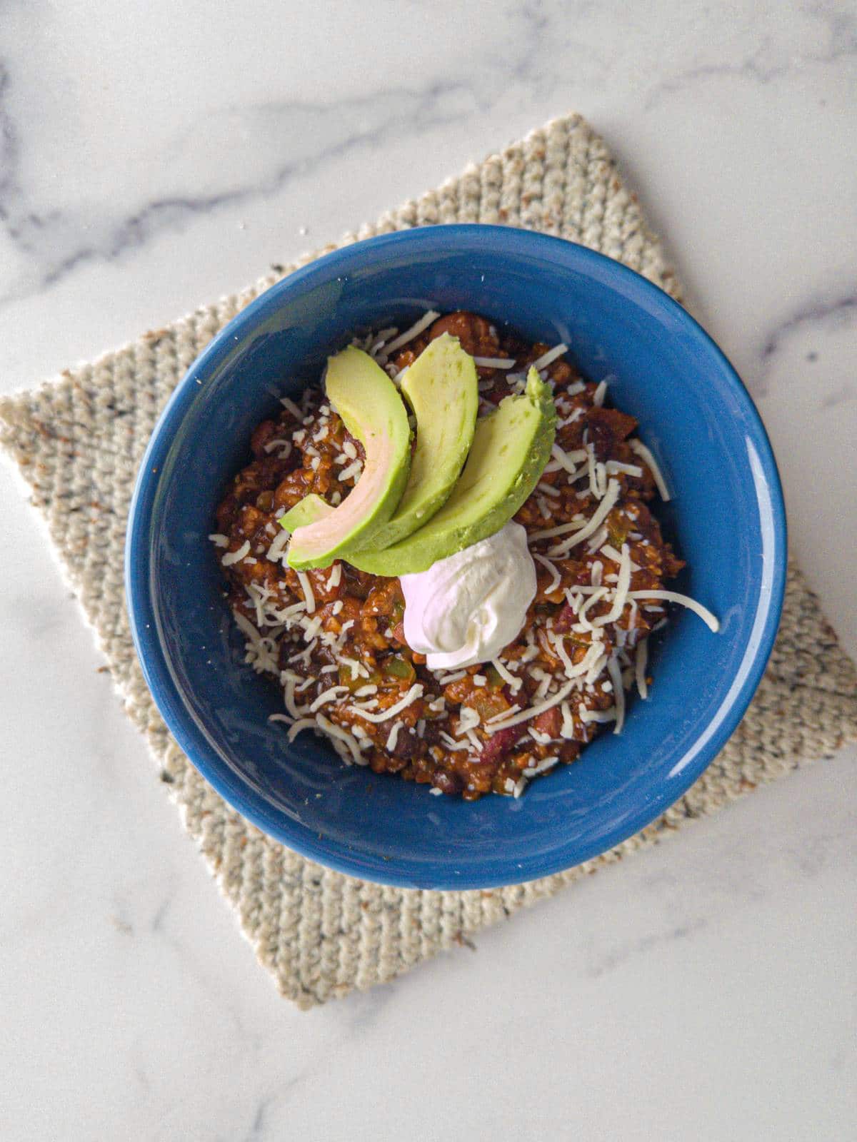 A bowl of thick and chunky chili topped with avocado.