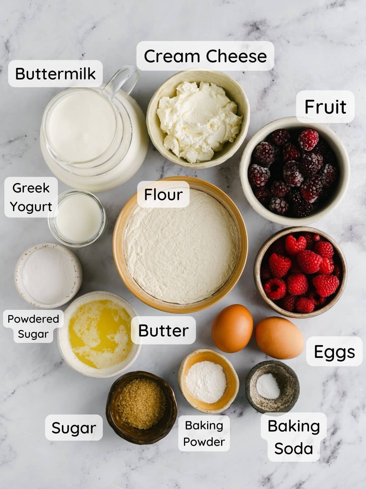 The pancake recipe ingredients on a table, with the text overlay "buttermilk, eggs, flour, sugar, baking powder, baking soda, melted butter, cream cheese, greek yogurt, powdered sugar, fruit."