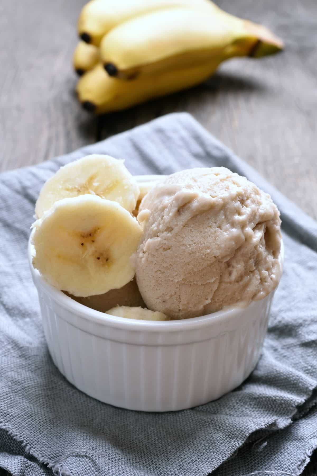 Fresh bananas and pudding with ice cream in a bowl with ripe bananas in the background.