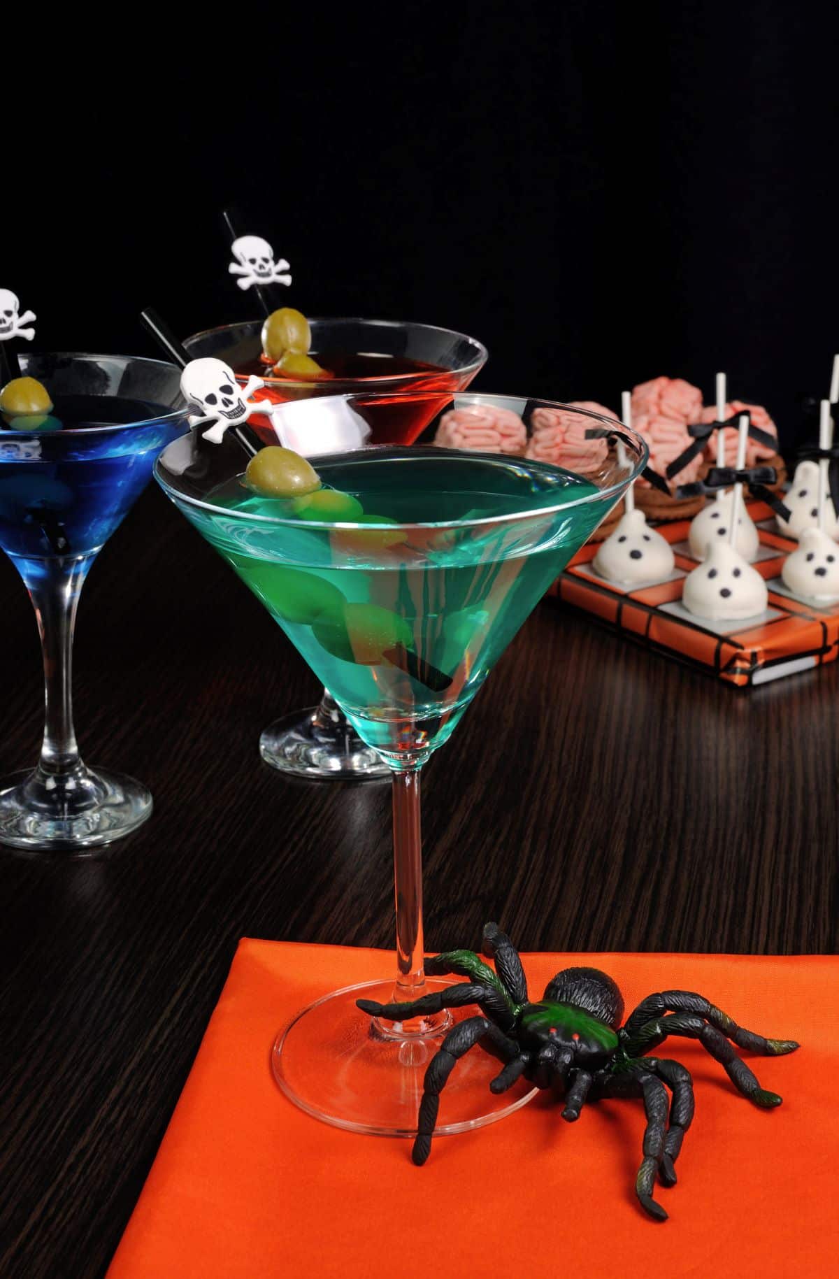 Several colorful halloween cocktails with spider garnishes.