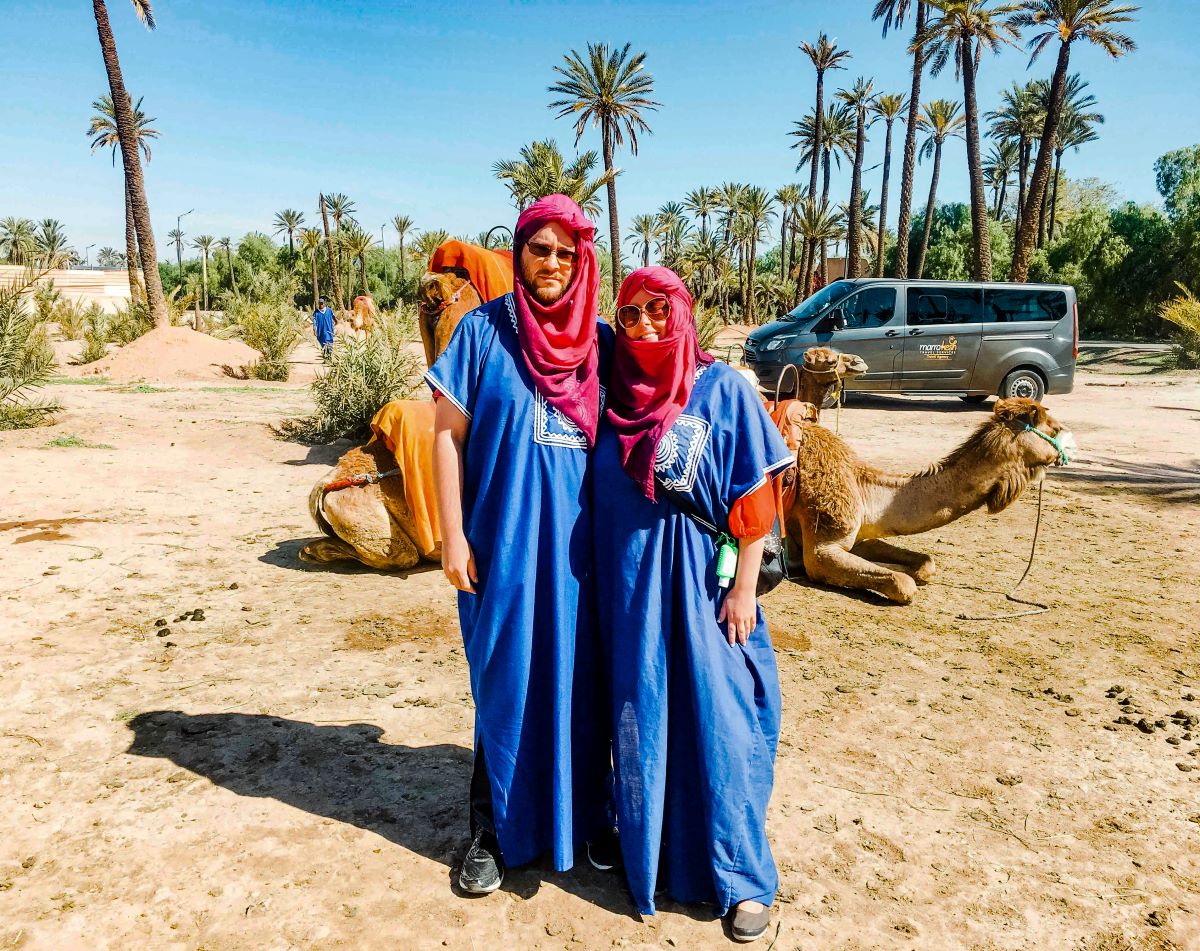 A couple in Marrakech in front of a camel that is lying down.